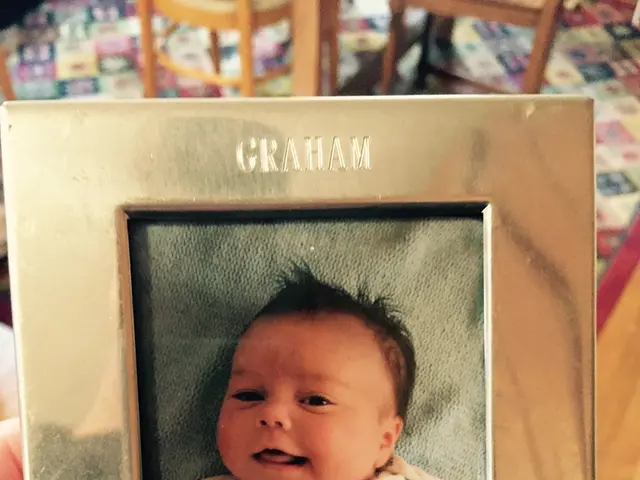 In this image we can see some person holding the photo frame of a boy and on the frame we can see...